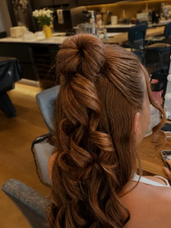 Auburn half up style with a full curled length, seen at the mirror